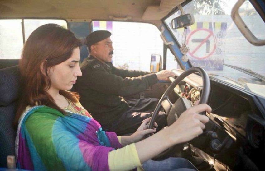 A woman in the driver's seat of a car with a police officer in the passenger street giving her instructions