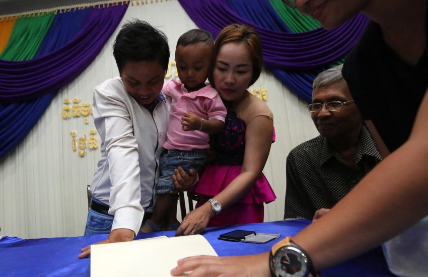 A couple holding a toddler put their fingerprints on a certificate as others look on smiling